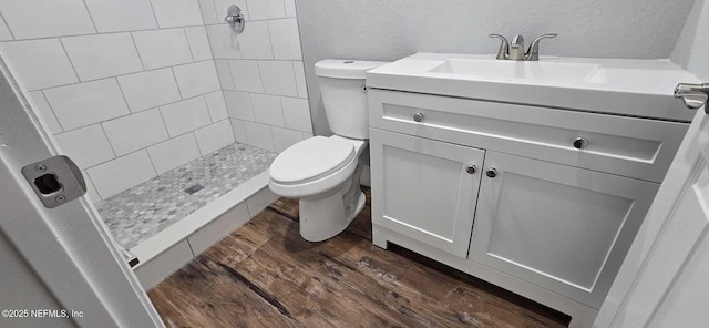 full bathroom with a textured wall, toilet, vanity, a shower stall, and wood finished floors