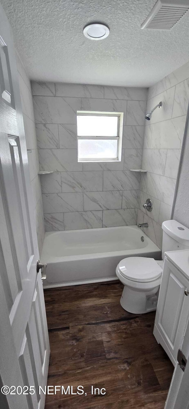 bathroom with a textured ceiling, toilet, wood finished floors, visible vents, and shower / washtub combination