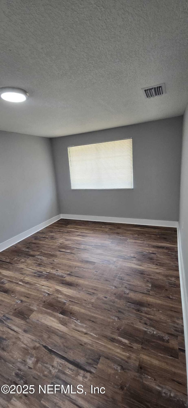 spare room featuring baseboards, a textured ceiling, visible vents, and dark wood-type flooring