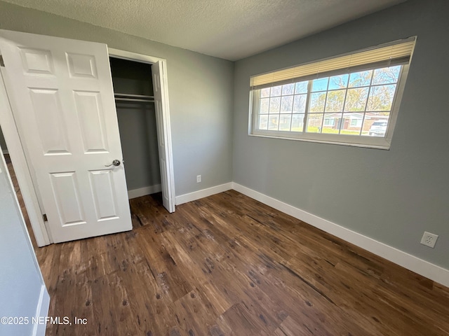 unfurnished bedroom with dark wood-style floors, a textured ceiling, a closet, and baseboards