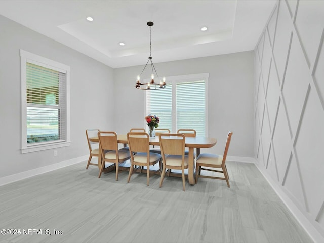 dining area featuring a tray ceiling, light hardwood / wood-style floors, and an inviting chandelier