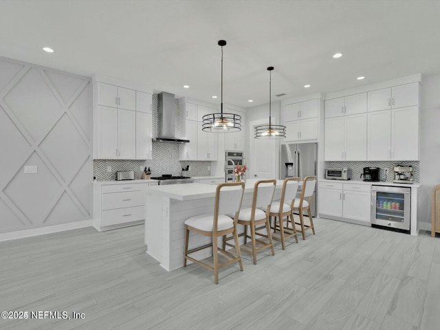 kitchen featuring pendant lighting, a center island with sink, wall chimney exhaust hood, appliances with stainless steel finishes, and beverage cooler