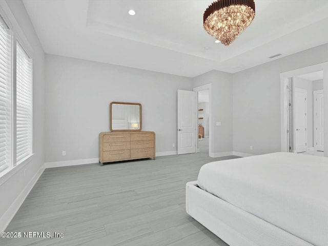 bedroom featuring a tray ceiling, a chandelier, and light wood-type flooring