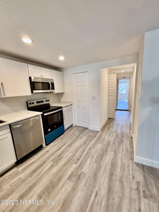 kitchen with decorative backsplash, appliances with stainless steel finishes, light hardwood / wood-style flooring, and white cabinetry