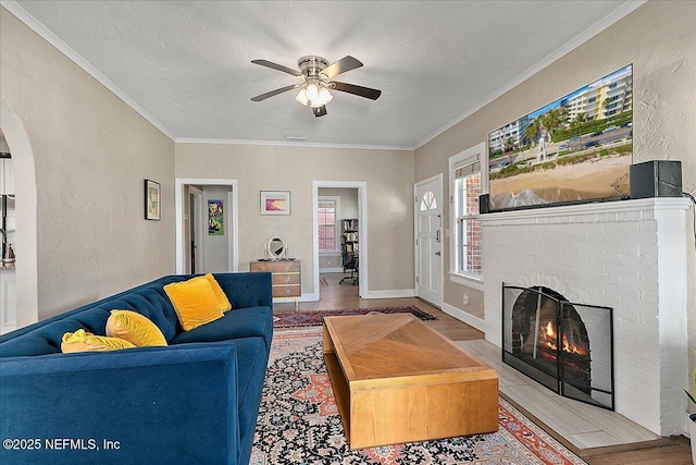 living room with ceiling fan, a fireplace, a textured ceiling, and ornamental molding