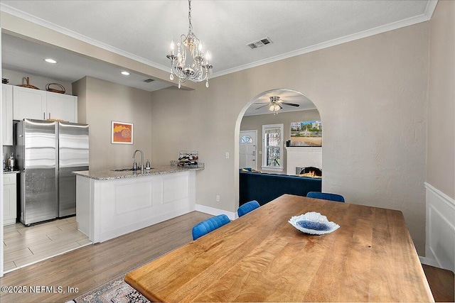 dining area with ceiling fan with notable chandelier, crown molding, and sink