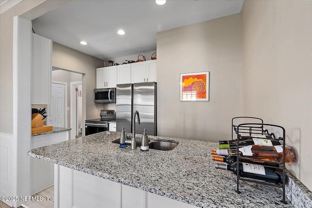 kitchen featuring kitchen peninsula, appliances with stainless steel finishes, light stone counters, sink, and white cabinetry