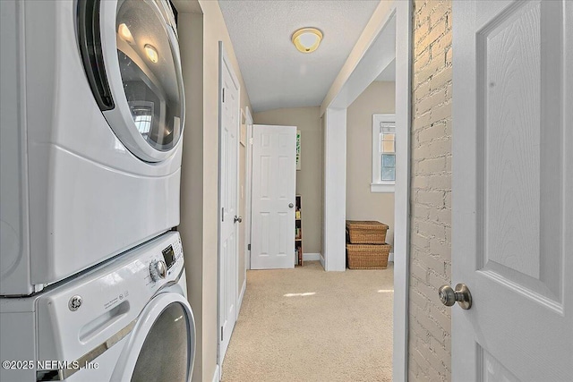 clothes washing area featuring a textured ceiling, stacked washer and dryer, and light carpet