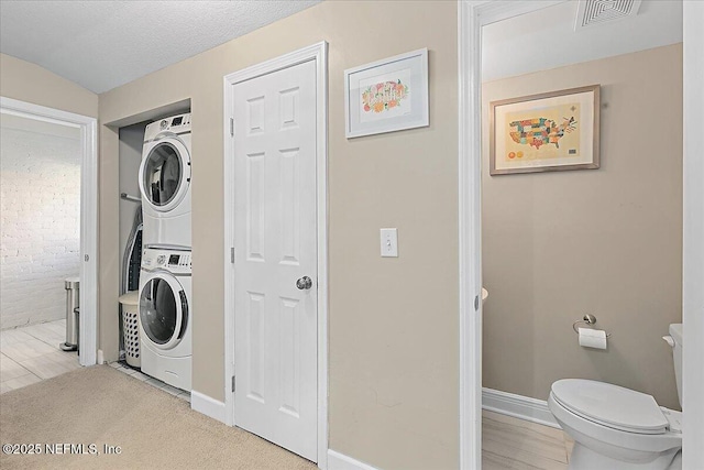 laundry area with a textured ceiling and stacked washer and clothes dryer