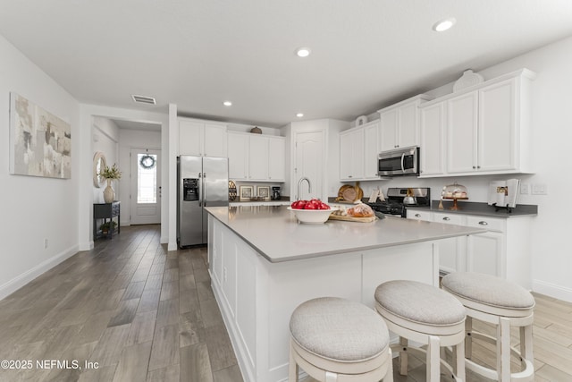 kitchen featuring appliances with stainless steel finishes, light hardwood / wood-style flooring, white cabinetry, and a kitchen island with sink