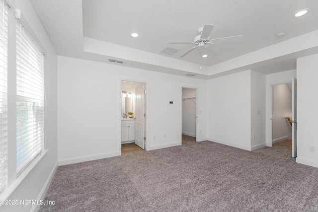 unfurnished bedroom with a walk in closet, a closet, a raised ceiling, and ceiling fan