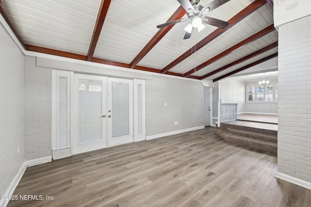 unfurnished living room with lofted ceiling with beams, wood-type flooring, ceiling fan with notable chandelier, and brick wall