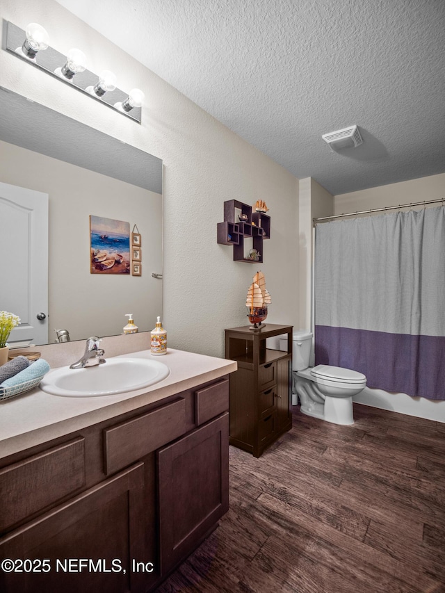 full bathroom featuring hardwood / wood-style floors, vanity, toilet, shower / bath combo with shower curtain, and a textured ceiling