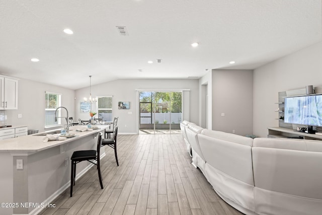 living room with plenty of natural light, sink, lofted ceiling, and light hardwood / wood-style flooring