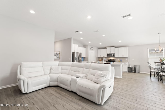 living room featuring sink, a chandelier, vaulted ceiling, and light hardwood / wood-style flooring