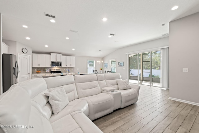 living room with lofted ceiling, a notable chandelier, light hardwood / wood-style floors, and a healthy amount of sunlight