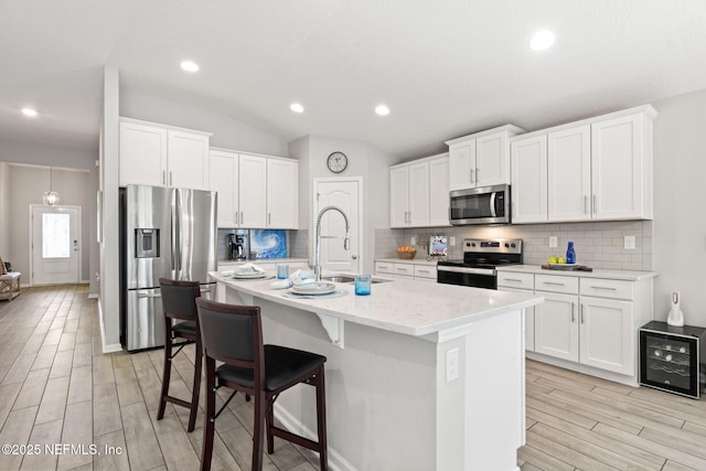 kitchen with stainless steel appliances, a kitchen island with sink, and white cabinets