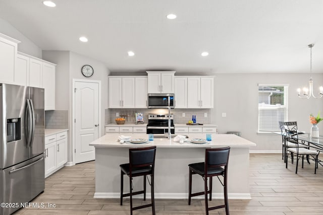 kitchen featuring an inviting chandelier, stainless steel appliances, white cabinets, a center island with sink, and decorative light fixtures