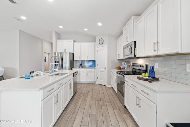 kitchen with appliances with stainless steel finishes, light stone counters, light hardwood / wood-style floors, white cabinets, and a center island with sink