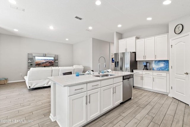 kitchen with an island with sink, sink, white cabinets, backsplash, and stainless steel appliances