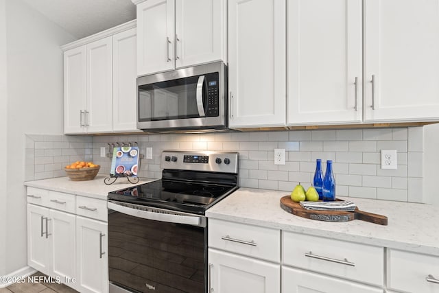 kitchen featuring stainless steel appliances, tasteful backsplash, white cabinets, and light stone counters