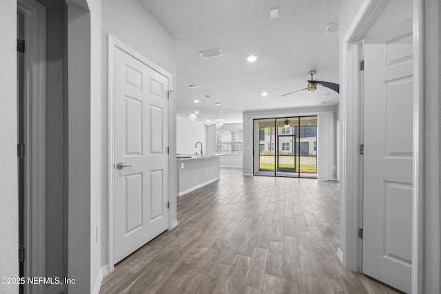 hallway featuring sink, light hardwood / wood-style flooring, and a textured ceiling