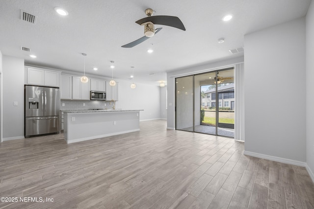 unfurnished living room featuring ceiling fan, sink, a textured ceiling, and light wood-type flooring