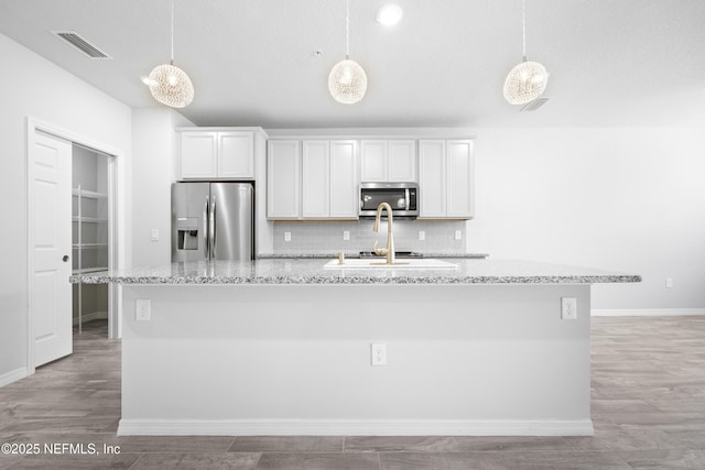 kitchen featuring hanging light fixtures, appliances with stainless steel finishes, a center island with sink, and white cabinets