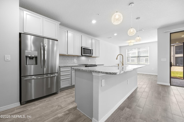 kitchen featuring pendant lighting, sink, white cabinets, stainless steel appliances, and a center island with sink