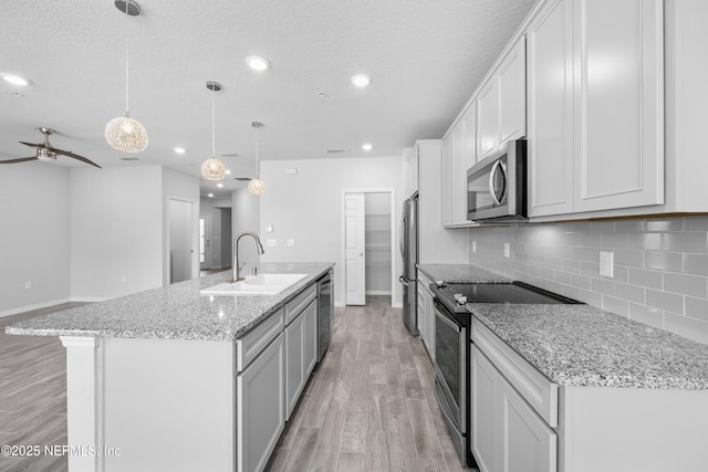 kitchen featuring sink, decorative light fixtures, appliances with stainless steel finishes, a kitchen island with sink, and white cabinets