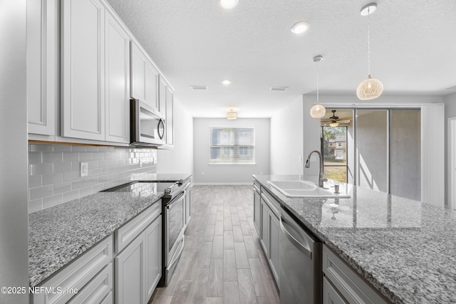 kitchen with sink, backsplash, hanging light fixtures, stainless steel appliances, and light stone countertops