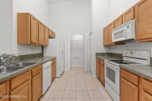 kitchen with dark countertops, a high ceiling, light tile patterned flooring, a sink, and white appliances