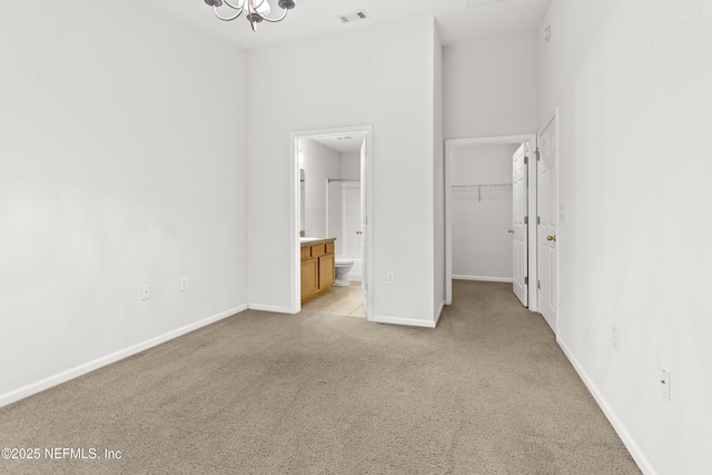 unfurnished bedroom with light carpet, a walk in closet, a chandelier, connected bathroom, and a closet