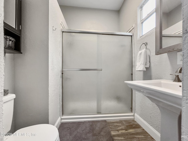 bathroom with hardwood / wood-style floors, toilet, and a shower with door