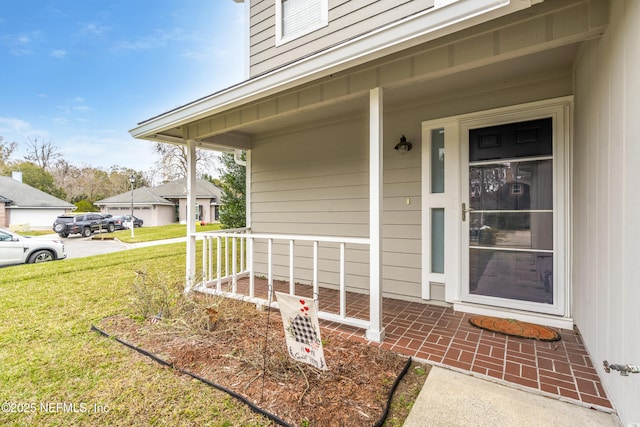 view of exterior entry featuring a lawn and covered porch