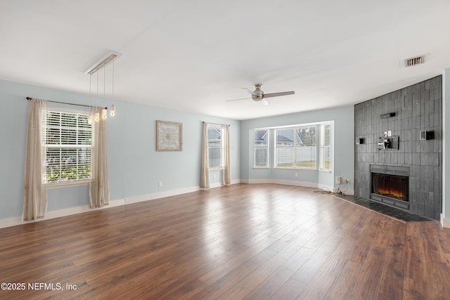 unfurnished living room featuring ceiling fan, wood-type flooring, a tiled fireplace, and a wealth of natural light