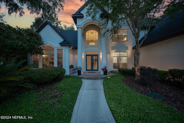 exterior entry at dusk with french doors and a lawn