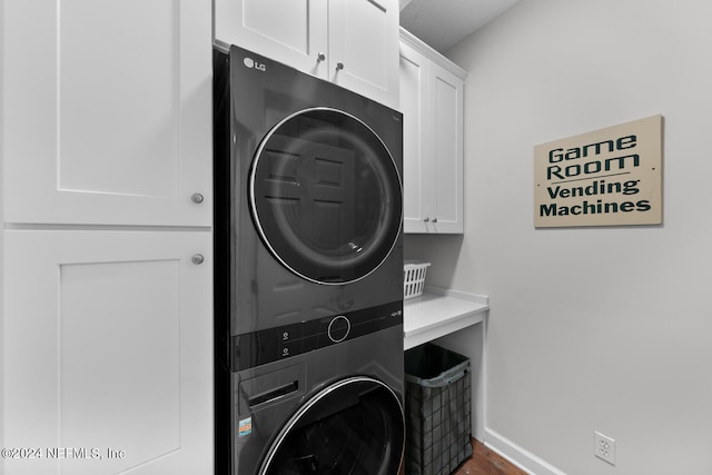 clothes washing area featuring stacked washer and dryer and cabinets