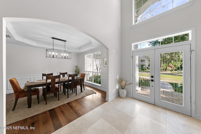 interior space with french doors, a wealth of natural light, a tray ceiling, and crown molding