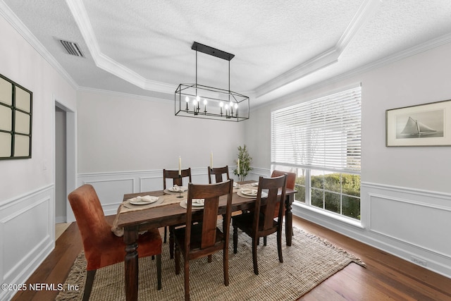 dining space with dark hardwood / wood-style flooring, a textured ceiling, ornamental molding, and a raised ceiling