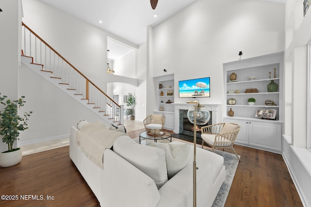 living room with a high ceiling, dark hardwood / wood-style flooring, built in features, and a fireplace