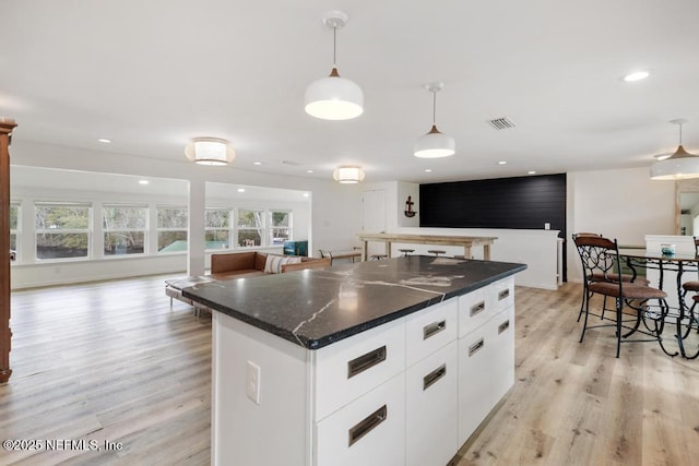 kitchen featuring white cabinetry, light wood-type flooring, dark stone countertops, a kitchen island, and decorative light fixtures