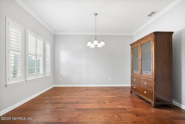 empty room featuring a notable chandelier, dark hardwood / wood-style floors, ornamental molding, and a textured ceiling