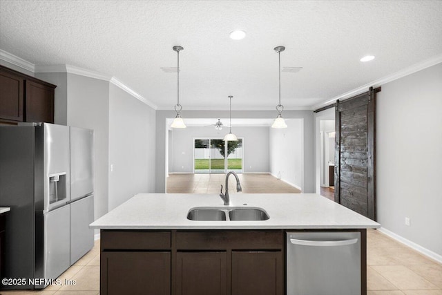 kitchen with a barn door, sink, stainless steel appliances, and an island with sink