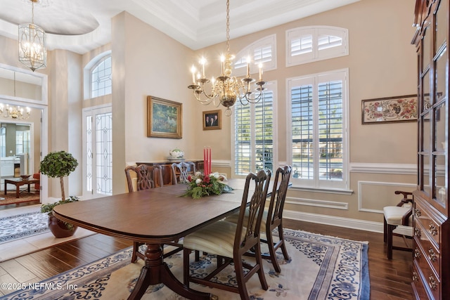 dining space with dark wood-type flooring, a towering ceiling, and an inviting chandelier