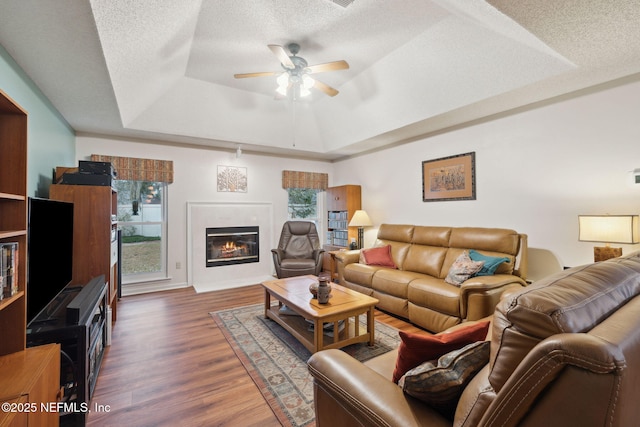 living room featuring a textured ceiling, ceiling fan, dark hardwood / wood-style flooring, and a tray ceiling