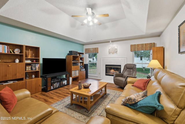 living room with ceiling fan, a tray ceiling, a textured ceiling, and light hardwood / wood-style flooring