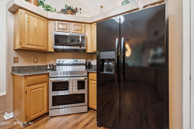 kitchen featuring appliances with stainless steel finishes, dark stone counters, light brown cabinets, and light hardwood / wood-style flooring