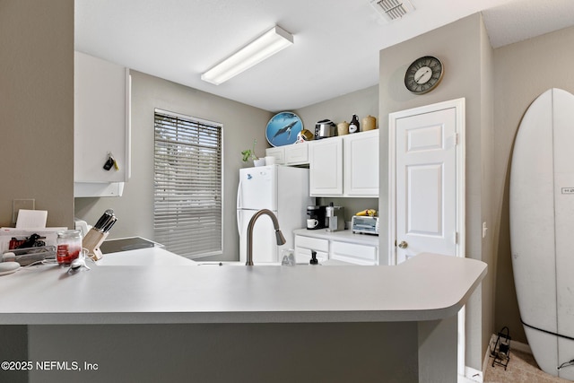 kitchen featuring white fridge, white cabinetry, kitchen peninsula, and sink