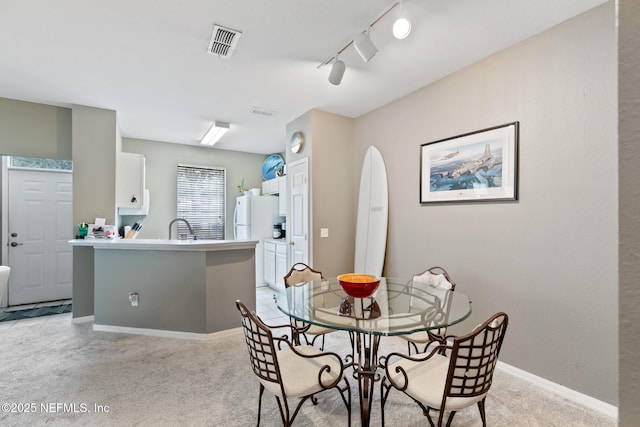 carpeted dining room featuring rail lighting and sink